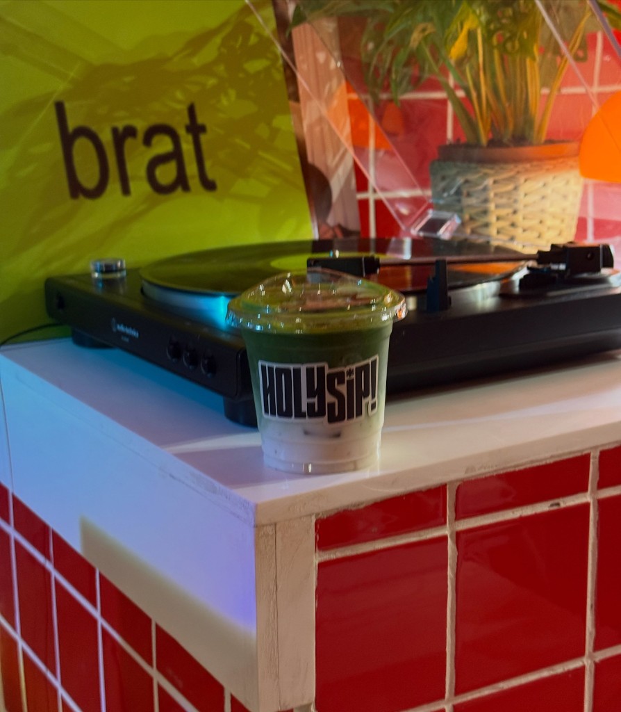 A layered iced matcha latte with a HOLYSIP! sticker in front of a record player.