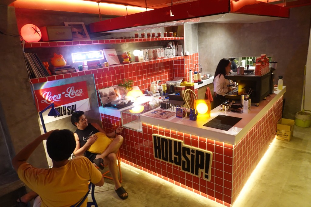 Holy Sip cafe counter with red tiles and a barista at the espresso machine.